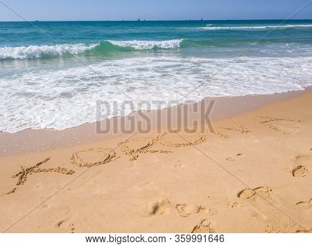 Korona Word Handwritten In Sand On Sunny Beach With Sun Sky Sea Background. The Text On The Sand, Th