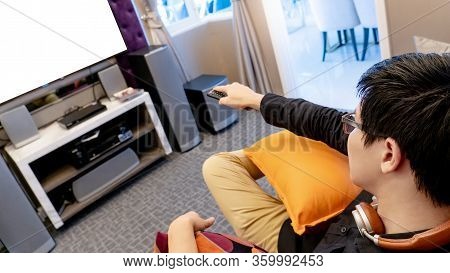 Asian Happy Man Using Remote Controller While Watching Tv Sitting On Sofa In Living Room. Domestic L