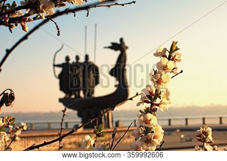 White Blossom Flowers On Tree Branch In Sunny Spring Morning. Blurred Silhouette Of Monument To Lege