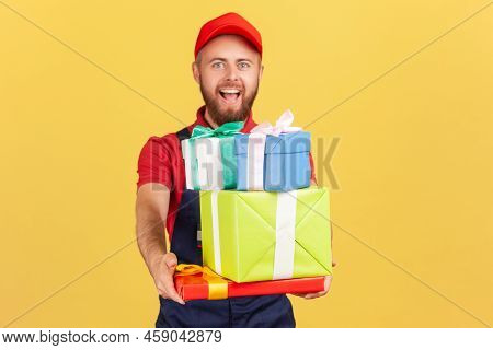 Portrait Of Excited Amazed Delivery Man Wearing Uniform And Red Cap Giving Many Gift Boxes To Client