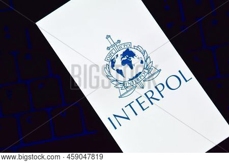 A Smartphone With The Interpol Logo Displayed On The Screen Lies On The Keyboard.
