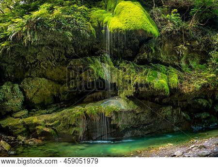 Small Waterfall Flowing Over The Cliff Face And Its Moss And Lichen In The Underground Gorge In Mart
