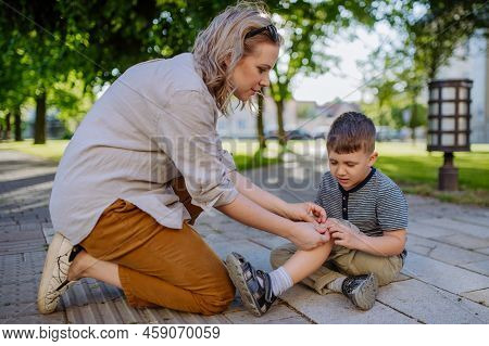 Young Mother Comforting Her Little Son And Giving Him Bandage After Getting Hurt When Fall Down In S