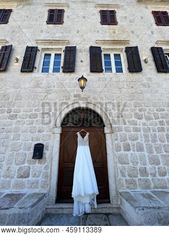 Wedding Dress Hangs Over The Door Of An Old Stone House With Shutters On The Windows