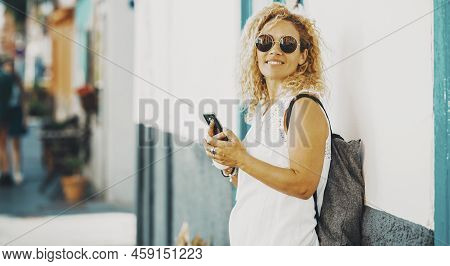 Happy Female Tourist Pose For A Picture Using Mobile Phone Connection Against A White Wall. Side Por