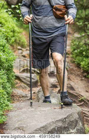 Muscular And Veiny Male Legs With Trekking Sticks For Nordic Walking On The Rocky Road In Mountains 