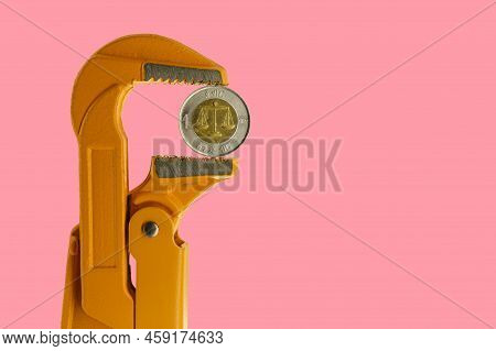 Ethiopian One Birr Coin Held In An Orange Plumber Wrench On A Pink Background. Reverse Of The Coin.