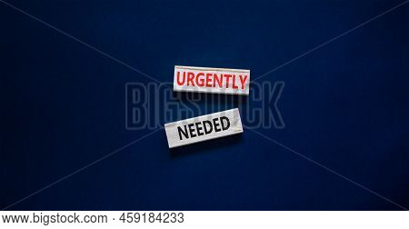 Urgently Needed Symbol. Concept Words Urgently Needed On Wooden Blocks On A Beautiful Black Table Bl