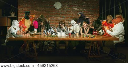 Group Of People Standing, Sitting At The Long Table In Different Costumes, Indoors And Lively Commun