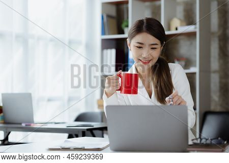 An Asian Female Employee Sits With A Red Coffee Mug In The Startup's Marketing Department Office, Sh