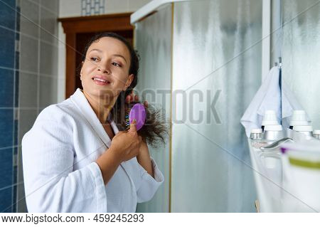 Beautiful Multiethnic Woman, In A White Waffle Bathrobe, Combing Hair, Looking Aside While Caring Fo