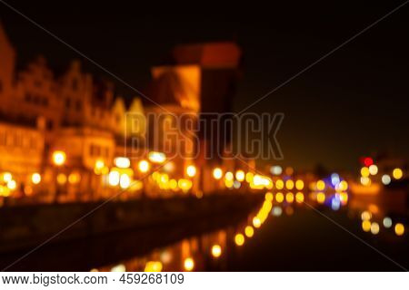 Defocused Photo Of Old Town In Gdansk At Night For Greeting Card Background. The Riverside On Granar