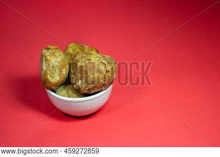 Closeup Of Indian Palm Jaggery Or Gur In A Bowl Isolated On Red Background With Copy Space In Horizo