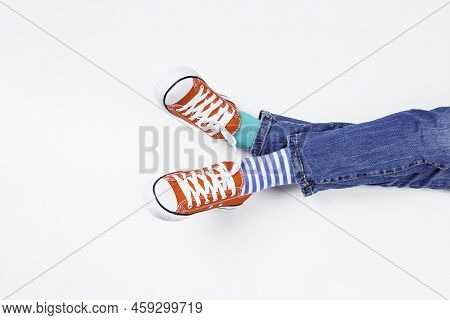 Kid Wearing Different Pair Of Socks. Child Foots In Mismatched Socks And Red Sneakers Sitting On Whi