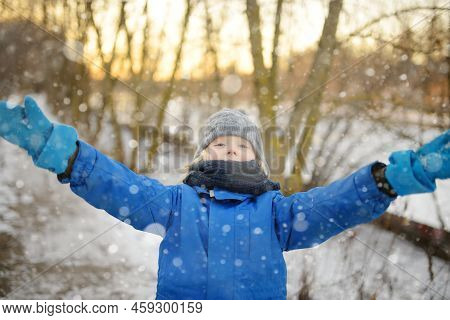 Portrait Of Funny Little Boy In Blue Winter Clothes Walks During A Snowfall. Cute Child Wearing A Wa