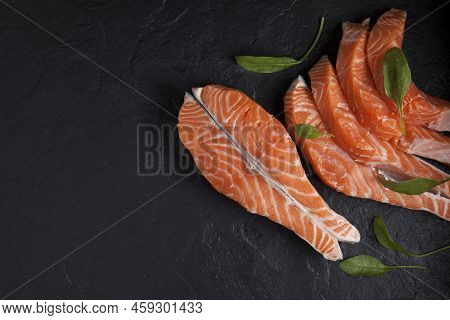 Steak And Slices Of Salmon Filet, Decorated With Spinach Leaves On A Black Textured Background. Clos