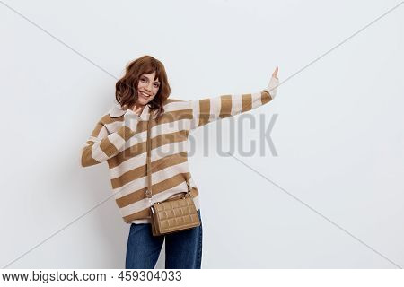 A Lovely Woman Stands On A White Background In A Striped Sweater And A Bag On Her Shoulder , Pulls H