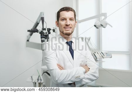 Happy Male Dentist In White Lab Coat Posing With Hands Crossed And Looking At Camera