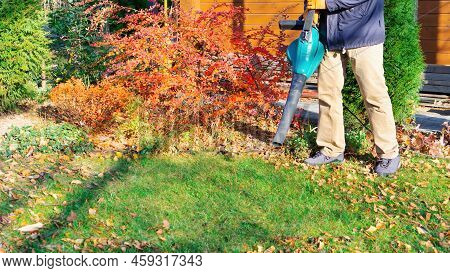 The Owner Of The Garden Cleans The Lawn From Fallen Leaves With An Electric Blower. The Gardener Cle