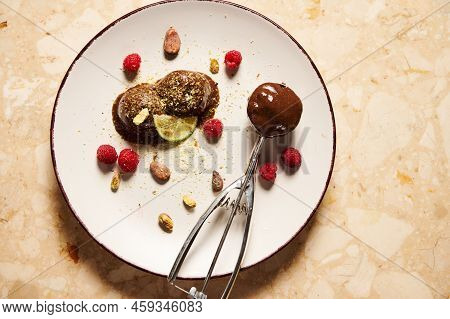 Flat Lay Of Frozen Chocolate Ice Cream Balls, Garnished With Pistachios, Raspberries And Slice Of Ju