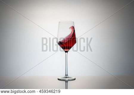 Movement Of A Crystal Glass Full Of Red Wine. Red Wine Glass Isolated On Grey Background With Reflec