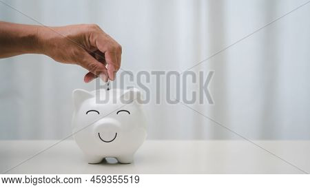 A Man's Hand Is Putting Coins Into A Piggy Bank To Save Money For Future Expenses, Financial And Mon