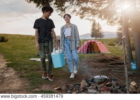 Happy Cheerful Couple Carrying Portative Fridge At Camping Site. Vacation In Mountains.