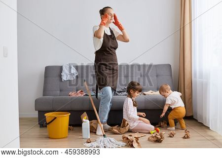 Image Of Tired Mother Standing Near Her Daughters, Mommy Cleaning At Home, Woman Touching Head, Kids
