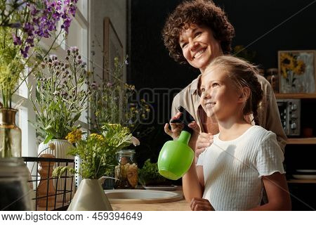 Happy Young Woman Standing Behind Her Cute Daughter Refreshening Flowers