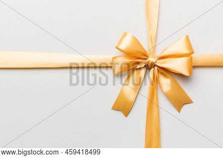 Top View Of Gold Ribbon Rolled And Yellowbow Isolated On Colored Background. Flat Lay With Copy Spac