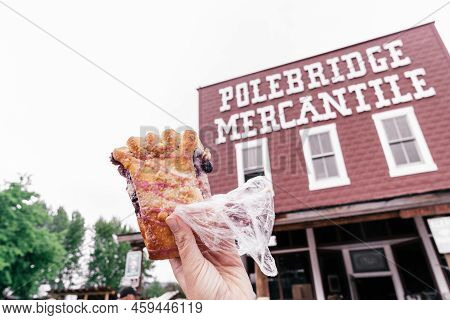 Polebridge, Montana - July 3, 2022: Hand Holds Up A Famous Huckleberry Bear Claw Pastery From The Me