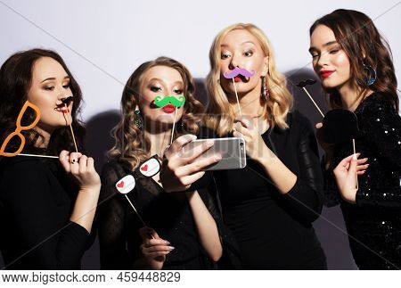 Four Charming Ladies Dressed In Black Cocktail Dresses With Party Falce Mustache Take Selfie.
