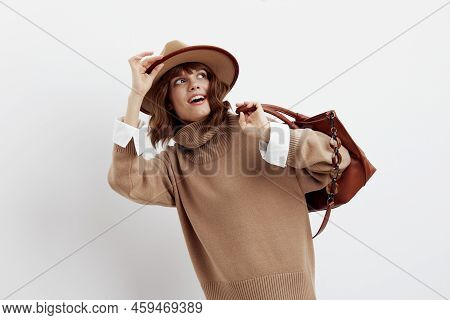 A Sweet, Happy Woman Stands On A White Background In A Beige Autumn Sweater And Holding A Bag On Her