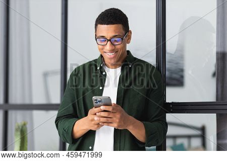 Young Smiling African American Man Relaxing Using Modile Phone Working In Modern Office