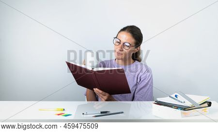 A Girl Reads A Book Or Textbook And Drinks Coffee - Study, Homework. High Quality Photo