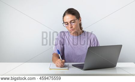 The Girl Sits At The Laptop And Makes Notes In The Notebook, Study, Work. High Quality Photo