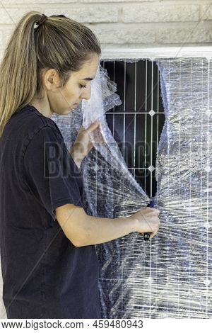 Close Up Vertical View Of Young Woman Unpacking The New Solar Panel From Bubble Wrap With A Cutter. 