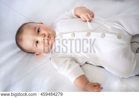 Cute Portrait Of A Baby In A Crib Close-up. A Child In White Clothes On White Underwear. Tenderness 