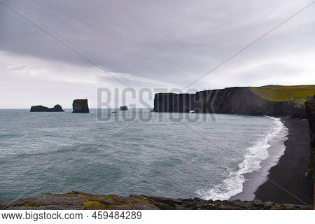 Vast Beach With Black Volcanic Sand With Coastline On The Atlantic Ocean And An Isolated Rock In The