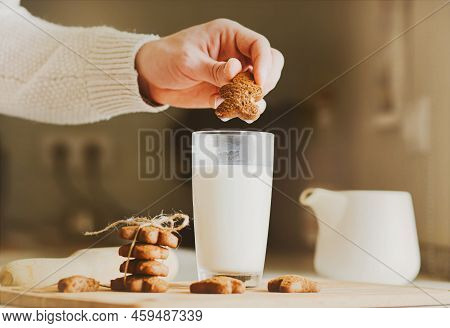 A Man In A White Wool Sweater Dunking A Gingerbread Man In A Glass Of Milk, And On The Table There A