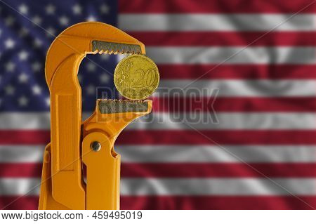 20 Euro Cent Coin Held In An Orange Plumber Wrench On The Background Of The Flag Of The United State