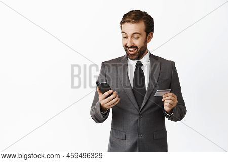 Enthusiastic Corporate Man Looking Pleased At His Phone, Smiling, Holding Credit Card, Receive Money