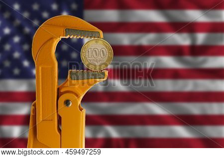 100 Kazakhstani Tenge Held In An Orange Plumber Wrench On The Background Of The Flag Of The United S