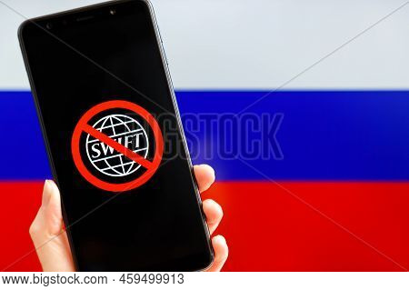 Ukraine, Kiev - February, 23 2022: Hand Holding Mobile With Crossed Out Swift Logo And Russian Flag 