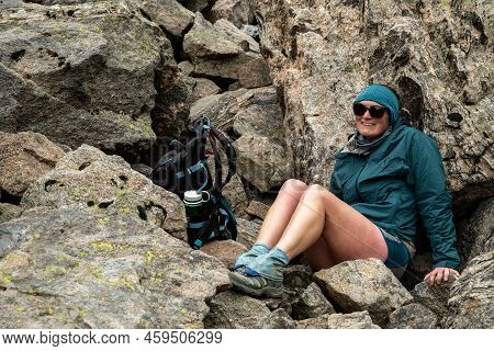 Woman Hunkers Down Behind Large Boulders From Cold Wind Along Trail In Rocky Mountain National Park