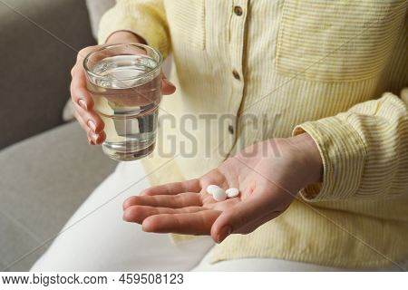 Calcium Supplement. Woman Holding Glass Of Water And Pills Indoors, Closeup