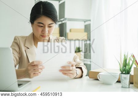Young Asian Female Freelan Sit Reading Report On Paper In Online Clothing Store..