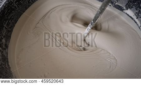 A Worker Using A Mixer Mixes The Self-leveling Floor In A Bucket. Stir The Solution In A Bucket. Bri