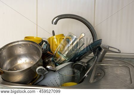 Dirty And Unwashed Dishes Are Stacked In The Kitchen Sink. Unwashed Cups, Plates, Pots, Forks And Sp