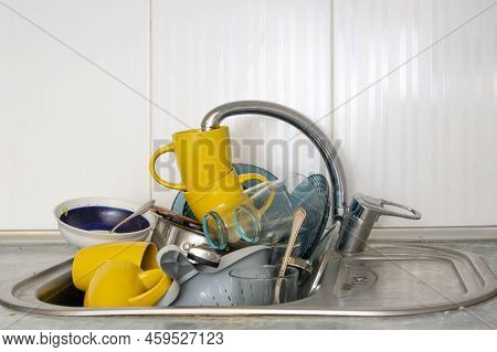 Dirty And Unwashed Dishes Are Stacked In The Kitchen Sink. Unwashed Cups, Plates, Pots, Forks And Sp